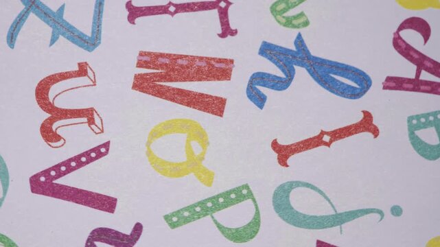 Close up pan of colorful jumbled alphabet pattern on white paper,  Playful typography background with scattered colorful letters
