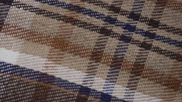 Rotating plaid fabric background with brown blue and beige checkered pattern, Top view of slow motion rotating tartan cloth texture in macro detail