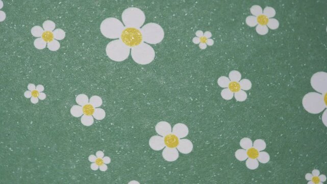 Rotating green background with white daisy flower pattern, Top view of slow motion rotating floral paper texture with daisies