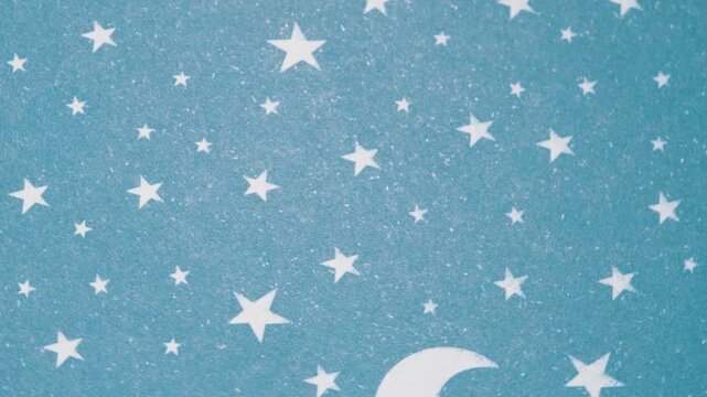 Rotating Celestial night sky background with white star shapes on teal paper texture, Top view of white stars and crescent moon pattern on blue textured paper
