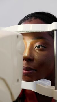 Vertical video, African woman having her eyes examined with a non-contact tonometer (NCT) for optical health