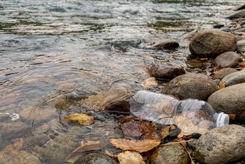 Plastic bottle floating among stones in shallow river water highlighting environmental pollution and plastic waste contamination in natural freshwater ecosystem landscape