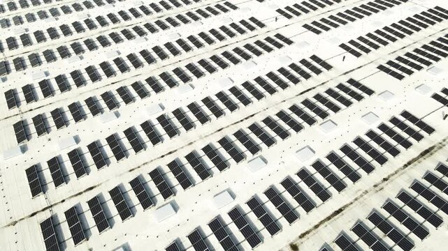Drone view of rooftop solar arrays on industrial building with sunset glow, visible wiring and spring snow patches.