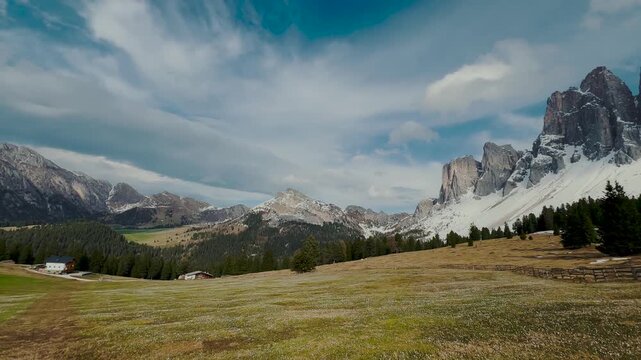 Spectacular jagged mountain peaks with snow patches above green meadow and wooden cabin, South Tyrol Dolomites, Italy
