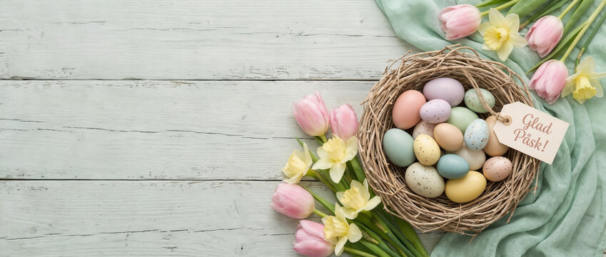 Glad P&aring;sk Swedish Easter greeting card with pastel eggs and spring flowers, rustic table and copy space