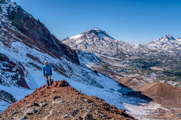A man stands on a rocky mountain top, looking out over a snowy landscape © ExploringandLiving