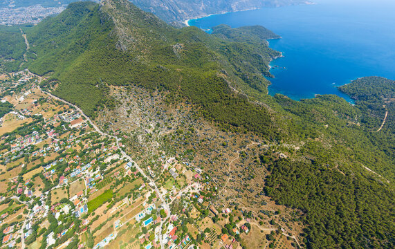Kayakoy, Turkey. Panoramic aerial photo of abandoned ghost town ruins and stone houses on mountain slopes under clear blue sky with bright sunlight. Aerial view