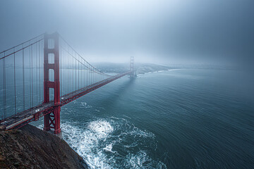 Fototapeta premium Golden Gate Bridge foggy morning over ocean with waves and rocky cliff coastline in panoramic view