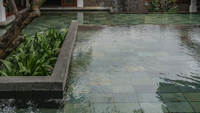 Decorative outdoor tropical pool. Turquoise tiled bottom. Green plants in a flower bed. Glare, reflection on clear water. Resort. Hotel