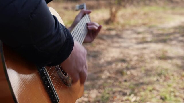 Close up hands of man playing acoustic guitar and singing relaxing enjoying outdoors on sunny autumn day. Artist learning and practicing playing musical instrument. Fall leaves autumnal weather 