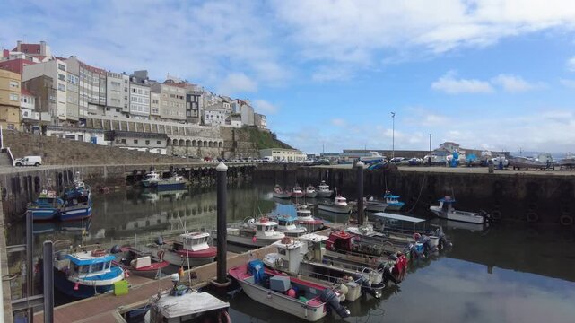 Picturesque view of the coastal town of malpica de berganti&ntilde;os in galicia, showing numerous fishing boats docked in the calm waters of the harbor on a partly cloudy day