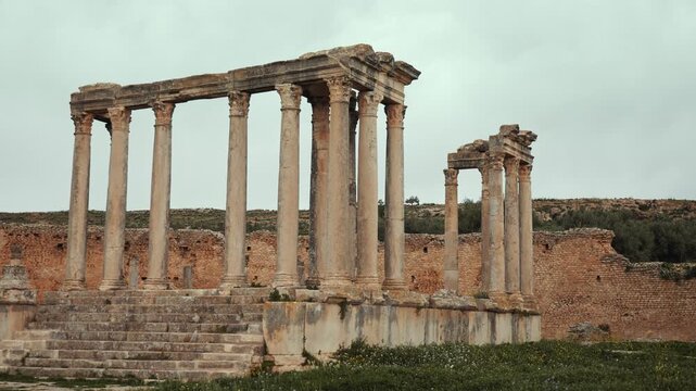 Remains of weathered stone steps and towering Corinthian columns of Roman Temple of Juno Caelestis among green fields