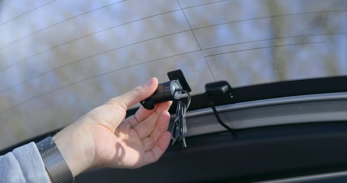 Close-up of hands installing a rear dashboard camera on the back window of a car, connecting the cable