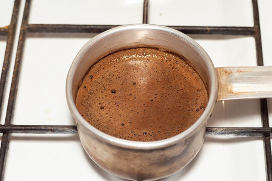 Aromatic freshly brewed coffee in a small metal cezve on a gas stove top during preparation