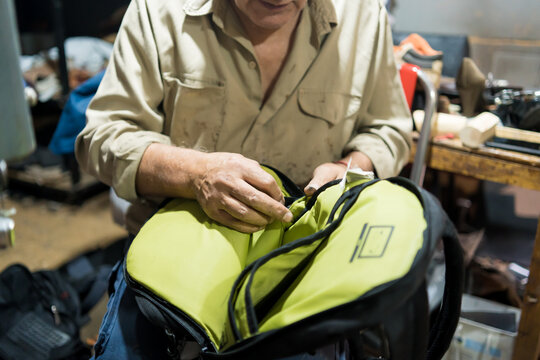 Close-up of hands of a cobbler repairing leather backpack in workshop, detailed craftsmanship and skilled artisan work
