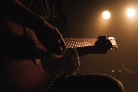Male musician playing acoustic guitar during rehearsal in a music studio for an entertainment blog, set against a dark stage with dramatic vintage lighting and copy space