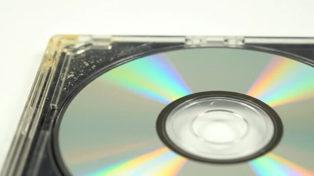 Close-up macro shot of a scratched CD in a cracked jewel case on white background