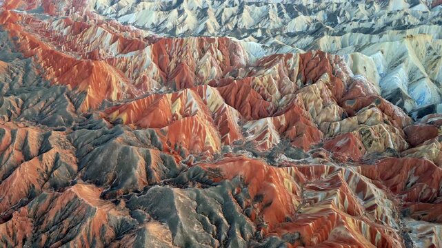 Aerial drone view of the colorful Zhangye Danxia Landform Geological Park in Zhangye, Gansu Province, China. Dramatic layered sandstone mountains display vibrant red, orange, and pastel mineral stripe