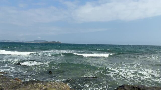 Clear ocean waves splashing against dark rocks under a blue sky. Filmed in 4K 120fps high frame rate with original sea wave ambient sound. Ideal for slow motion.