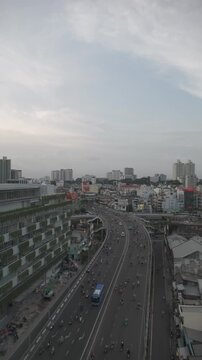 Aerial drone view of heavy motorbike traffic moving along elevated highway through dense urban district with buildings and city skyline in Ho Chi Minh City Vietnam