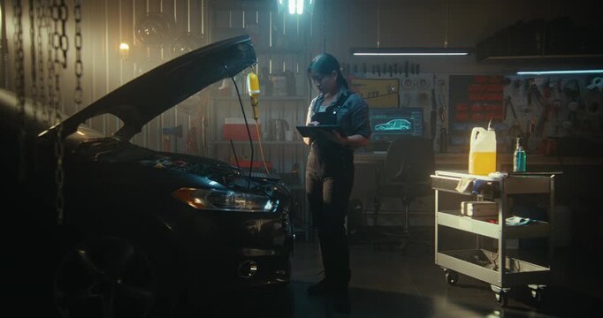 Female Auto Mechanic Connects Laptop to Car Engine For Advanced Computer Diagnostics. Holding Tablet, Girl Uses AI Powered System to Analyze Data and Compare Results With Baseline Performance Metrics.