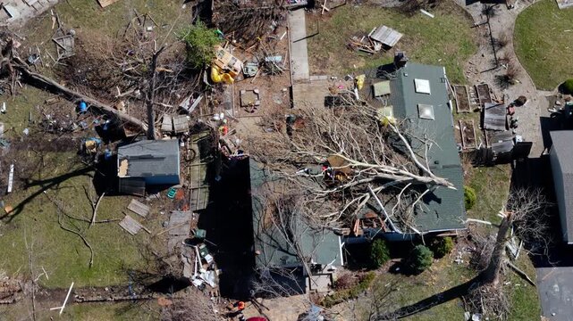 Aerial view of tornado destruction in a suburban area with damaged houses. trees on roof and widespread debris.