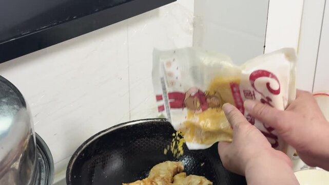 Cooking food in a wok at home kitchen, with pieces of battered ingredients deep frying in hot oil while being stirred with a metal spatula, showcasing energetic Chinese home cooking in Xi'an, China.