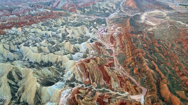 Aerial drone view of Zhangye Danxia National Geopark, Zhangye, Gansu, China. Winding desert road cuts through multicolored striped hills while hot air balloons prepare for launch near the scenic viewp