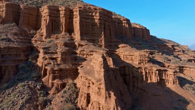 Dramatic rock formations rise majestically in arid mountainous terrain of Kyrgyzstan. Clear blue sky enhances the ancient, desolate landscape.