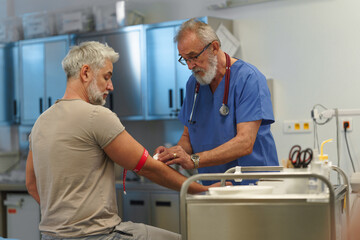 Older doctor drawing blood from patient's arm.