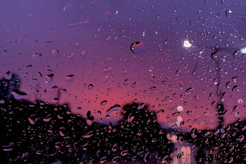 Fototapeta premium Raindrops on window with a moody purple and pink twilight cityscape