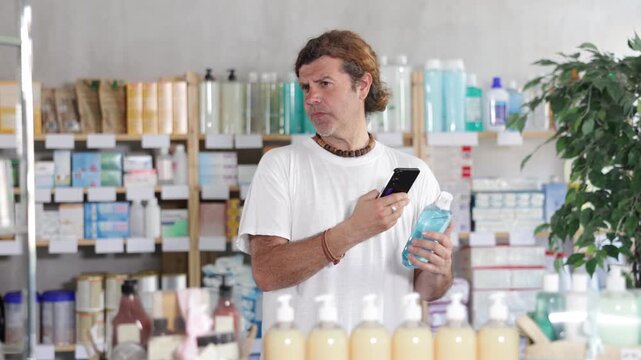 Man stands in a pharmacy in the summer and scans the barcode of a mouthwash on his phone to read detailed instructions on the manufacturer's website. High quality 4k footage