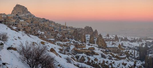 Snow covered Uchisar Castle overlooking Cappadocia village at sunset