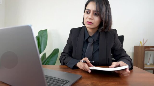 Closeup of frustrated upset working young Asian businesswoman manager sits on chair at workplace desk hold pen and book looking at laptop screen online data analysing network issue feels depressed.