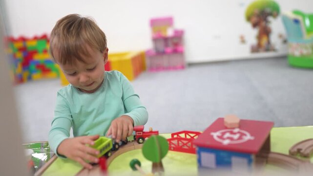 Young child playing with toy train. Boy, plays, railroad, toys carriages, train, son. A train with carriages and a boy playing with it. The photo is lifestyle of a child playing with a toy train.