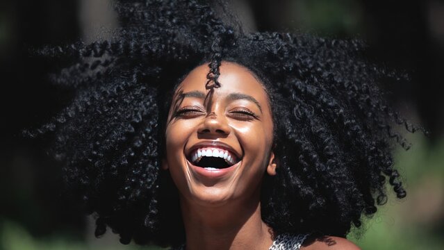 Joyful african female young adult with curly hair laughing outdoors.