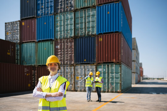 Portrait of confident female worker in front of colleagues and cargo containers on industrial site