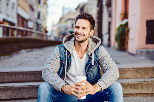 Man with coffee sitting on stairs with city in background