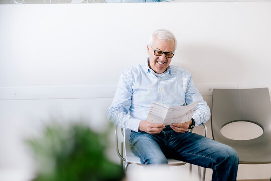 Senior man sitting in waiting room of medical practice, reading leaflet