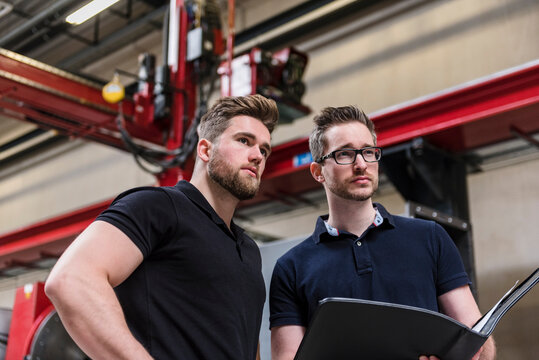 Two men with folder on factory shop floor looking around