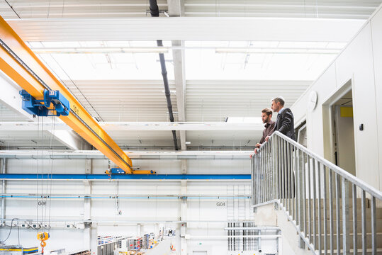 Two businessmen standing upstairs in a factory