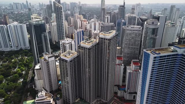 Drone flyover at rooftop height passes through dense Makati office and residential towers revealing facade patterns rooftop structures and a layered daytime skyline deep into the district