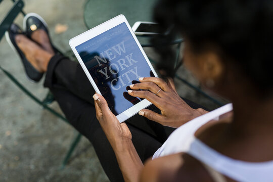 USA, New York City, woman sitting in a park using travel guide on tablet