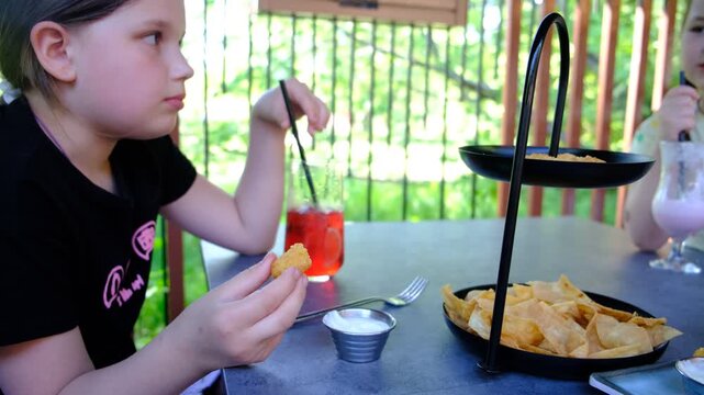 Two sisters, pretty girls eating Squid rings, crispy snack, cheese sticks, drinking milkshakes, red fruit mint cocktail. Happy children in the cafe, street food. Kids having lunch. Activity and leisur