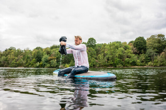 Wet businessman sitting on SUP board on a lake