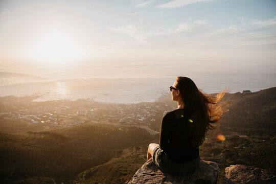 South Africa, Cape Town, Kloof Nek, woman sitting on rock at sunset