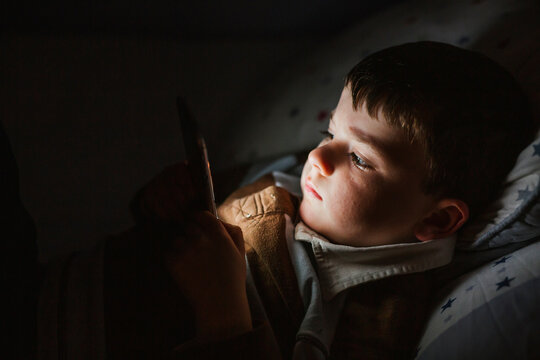 Portrait of little boy lying in bed using smartphone at night