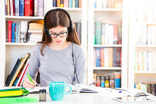 Girl listening music with headphones while doing homeworks