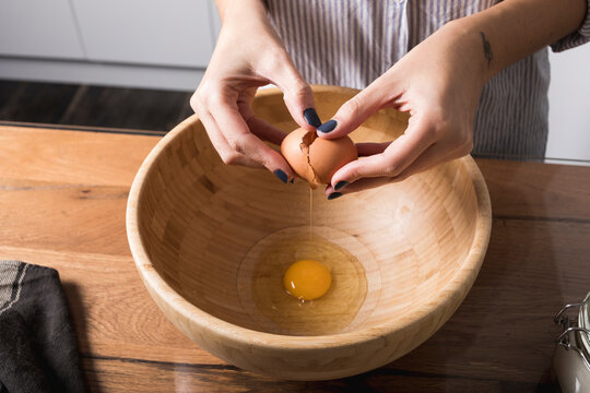 Woman breaking egg, wooden bowl