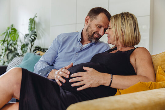 Mature man and his pregnant mature wife sitting on couch touching her belly